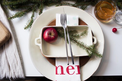 Ett lite grövre porslin i vitt ger rustik känsla. Välj udda servetter med mönster i rött och vitt. Vik servetten till en ficka, lägg i bestick och fäst namnlappen med ett snöre runtom, dekorera med en grankvist. En sprayad sked med namn på.